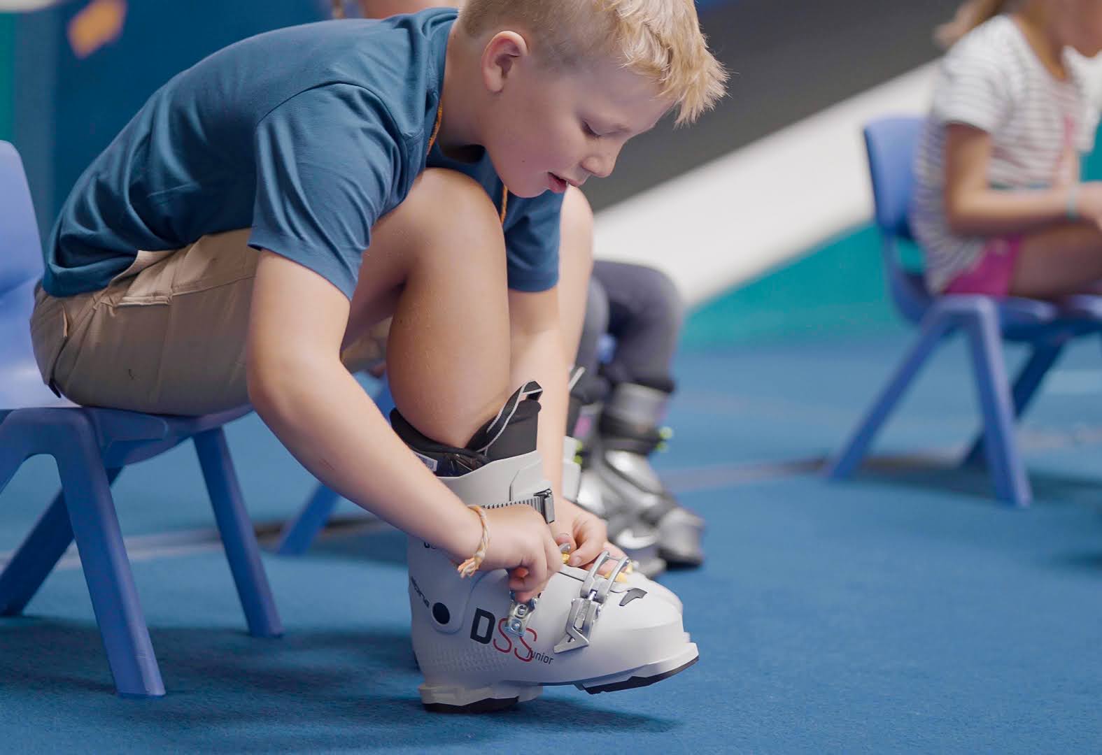 Boy at Shredder bending to buckle his own ski boot, an intimate prep moment