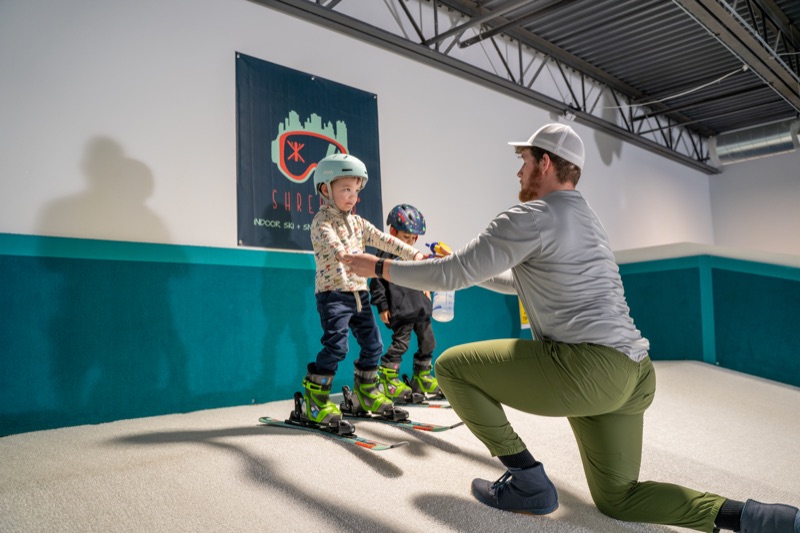 Instructor kneeling with two young kids in helmets at Shredder Chicago