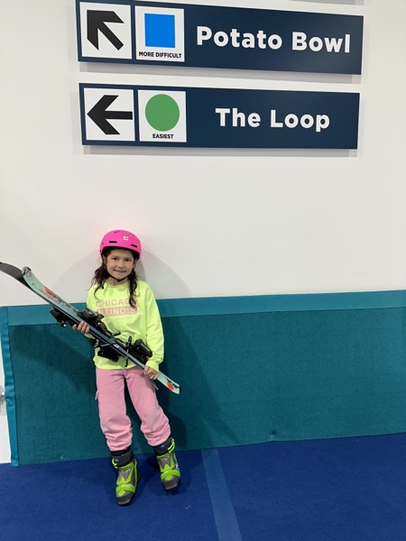 Girl posing with skis under Potato Bowl and The Loop trail signs at Shredder Chicago