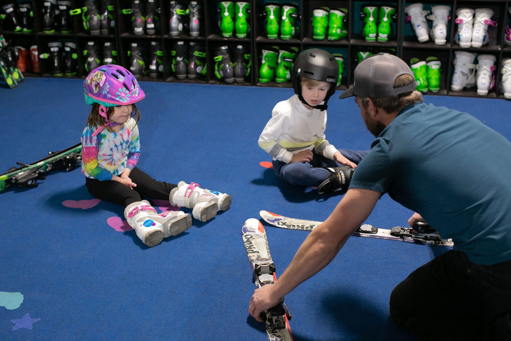A coach fitting ski boots for two young children at Shredder Central Park