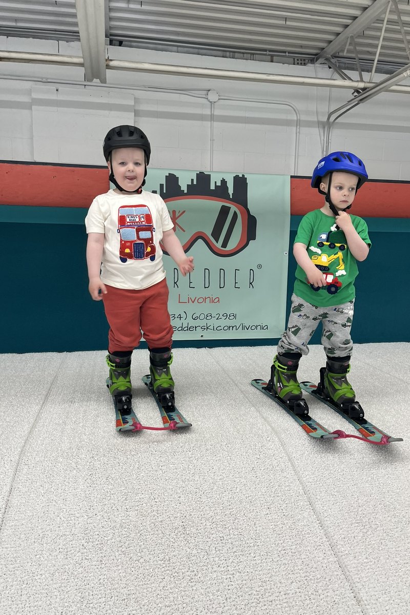 Two young skiers standing in front of the Shredder Livonia banner