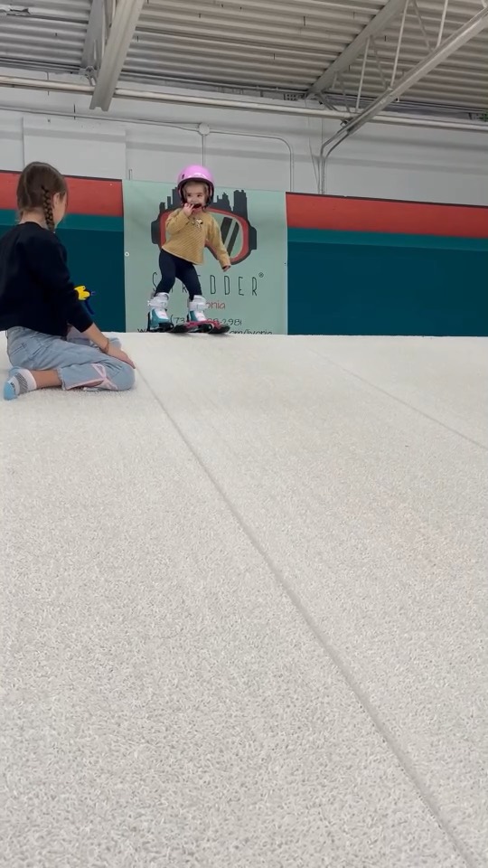 A toddler skiing toward a kneeling coach at Shredder Livonia