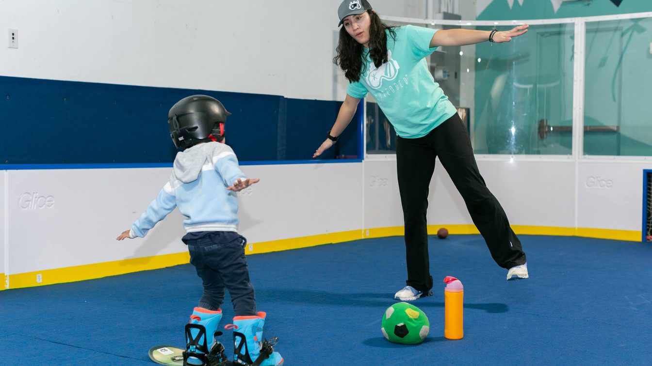 A coach showing a young rider how to stand on a board, at Shredder