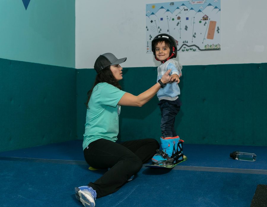 A coach kneeling to steady a small child on the slope