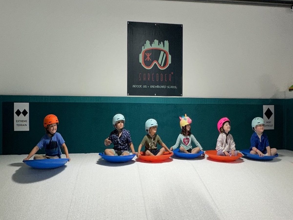 Six children sitting on saucers in a row under the Shredder sign