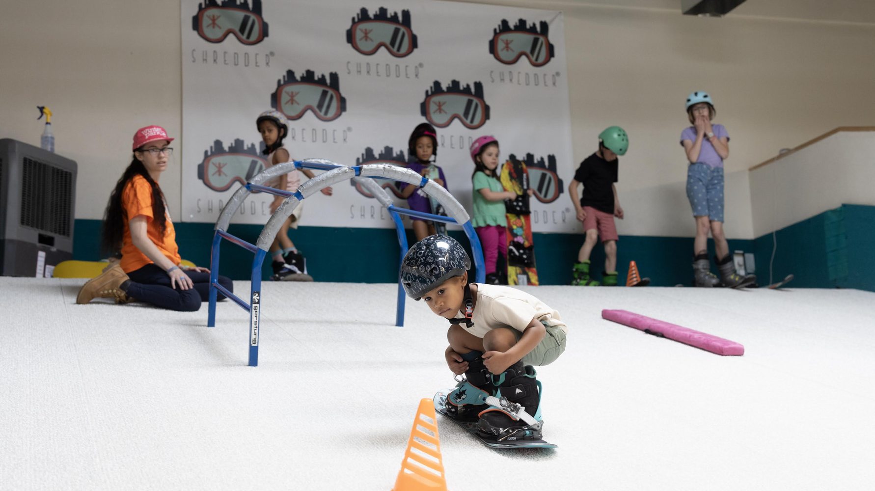 A young rider steering a snowboard through cones on the indoor slope