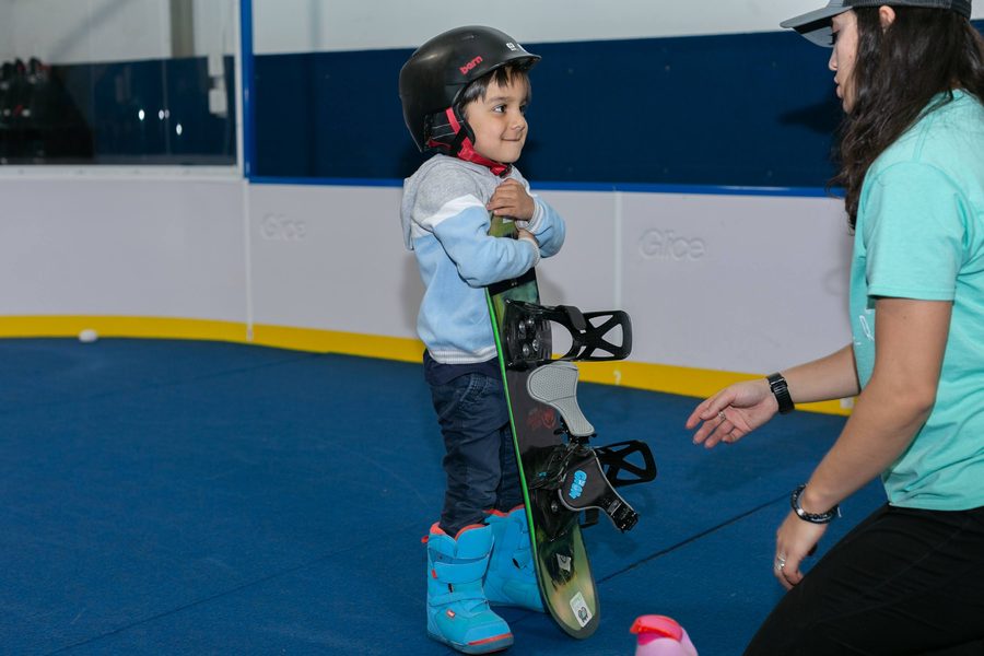 A coach greeting a small child holding a snowboard