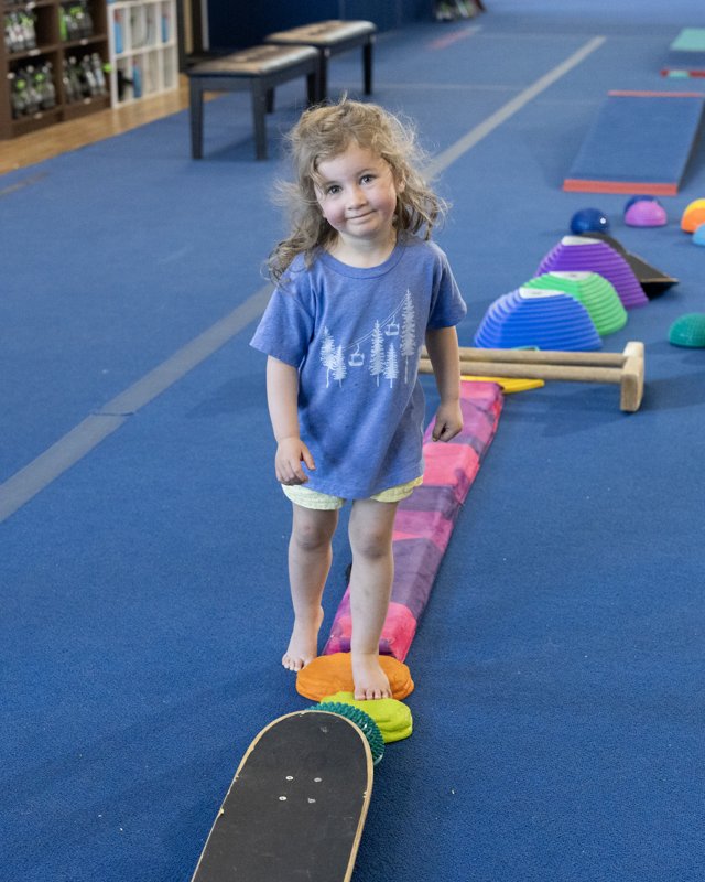 A smiling toddler walking a balance trail of soft beams and pods on the play floor