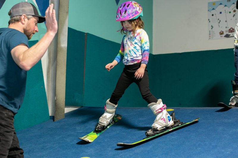 A Shredder coach kneeling face to face with a small child on a snowboard