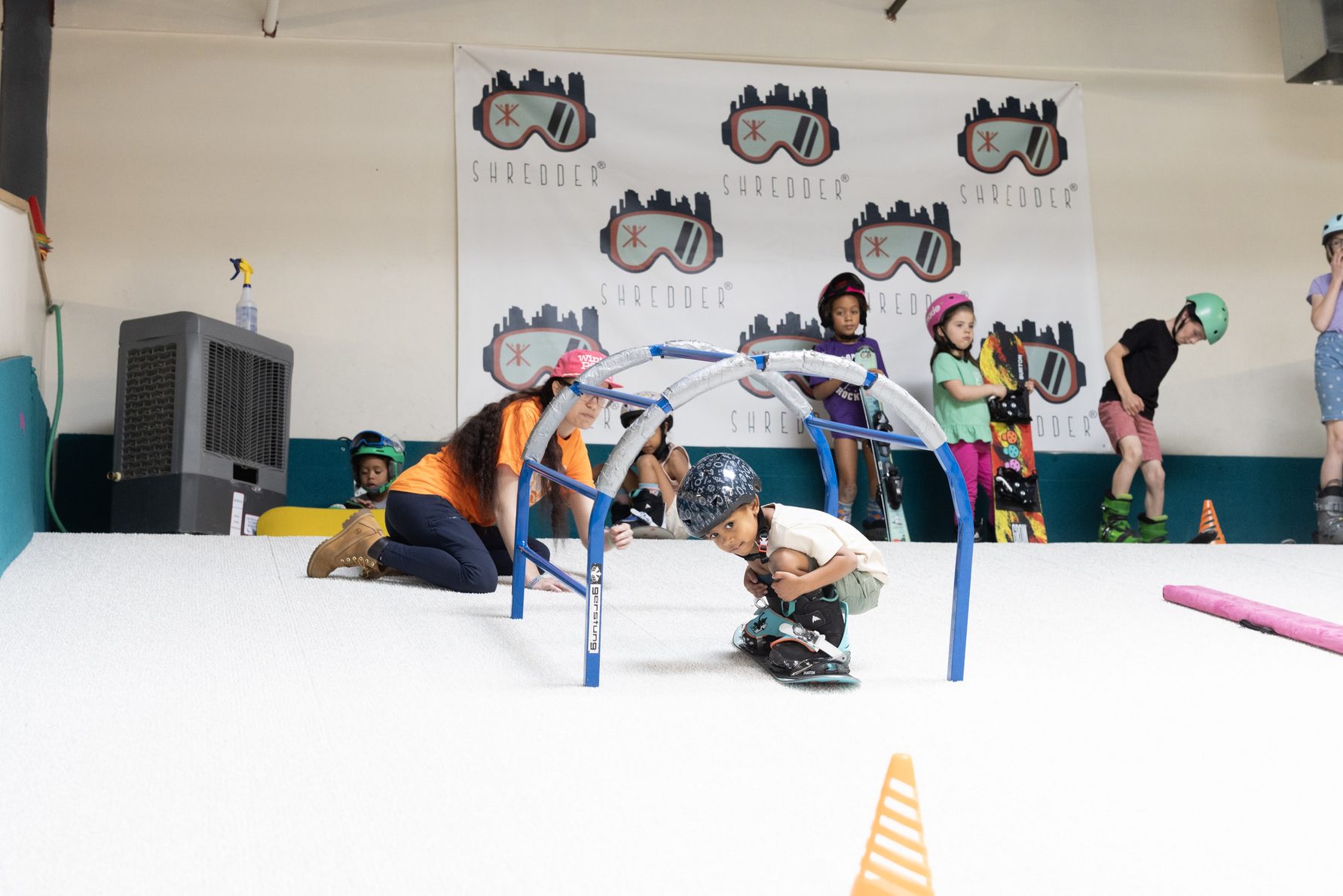 A coach helping a young snowboarder through a training arch at Shredder Wheat Ridge